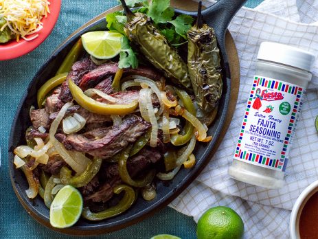 Texas-style fajitas served in a cast iron skillet with jar of Fiesta Fajita Seasoning.