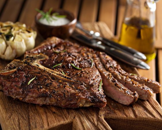 Uncle Chris Gourmet Steak on cutting board with head of roasted garlic in background