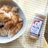 Seasoning the chicken wings using Fiesta Brand Wing Tips seasoning. Coating wings evenly and tossing them in a bowl before placing over hot coals on a backyard BBQ pit.