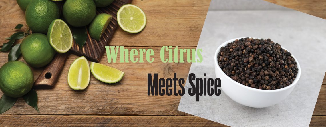 Overhead view of fresh limes and lime wedges on wooden surface beside black peppercorns
