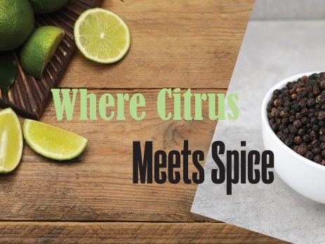 Overhead view of fresh limes and lime wedges on wooden surface beside black peppercorns